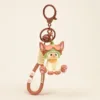 Cute cat keychain with Devon label, wearing green strawberry hat, brown bell and paw accessories