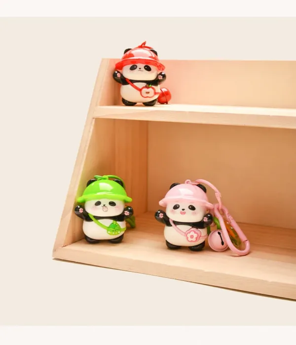Three cute panda figurines with colorful hats on wooden display shelves, pink one has keychain