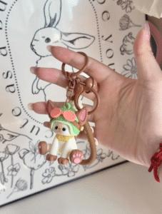 Hand holding cute cat keychain wearing green helmet with goggles and pink bow