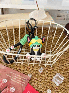 Cute black and white cat keychain wearing green aviator helmet in white wire basket