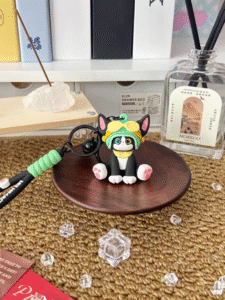 Cute black and white cat keychain figurine wearing yellow goggles on wooden tray