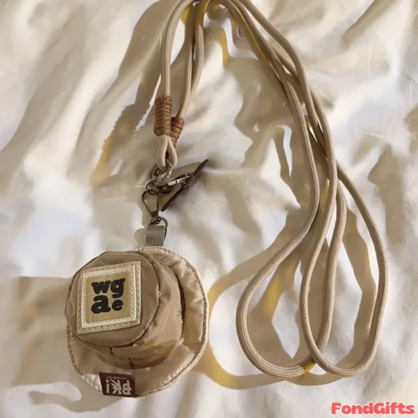 Beige round mini pouch with wgae logo on lanyard strap laying on white fabric