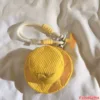 Yellow Corduroy Mini Hat Keychain with Rope Strap Accessory Yellow corduroy mini bucket hat keychain with white rope strap, silver carabiner clip, and orange airplane charm on fabric