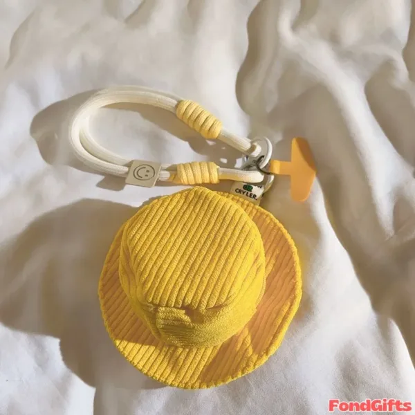 Yellow Corduroy Mini Hat Keychain with Rope Strap Accessory Yellow corduroy mini bucket hat keychain with white rope strap, silver carabiner clip, and orange airplane charm on fabric