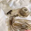 Clear phone case with crossbody lanyard strap, mini beige pouch with zipper, and brown braided keychain on white fabric