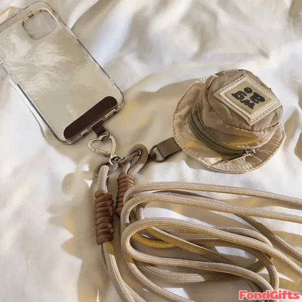 Clear phone case with crossbody lanyard strap, mini beige pouch with zipper, and brown braided keychain on white fabric