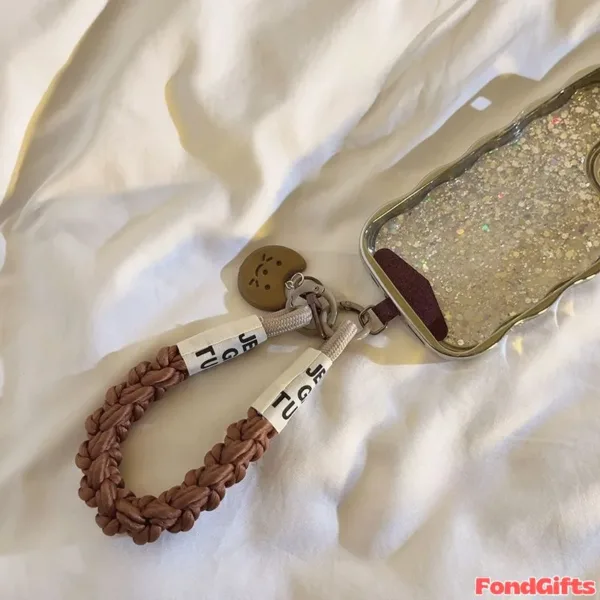 Glitter phone case with braided brown leather wrist strap and smiley face charm on white bedding