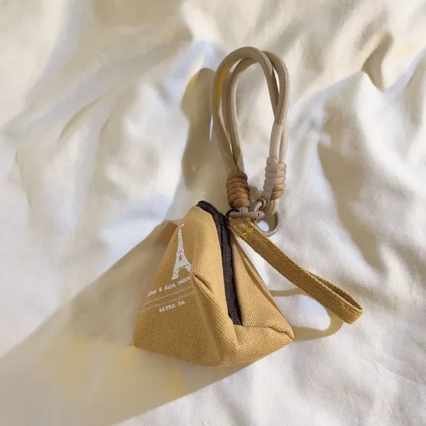 Small tan canvas pyramid coin purse with Eiffel Tower print and rope strap on white fabric