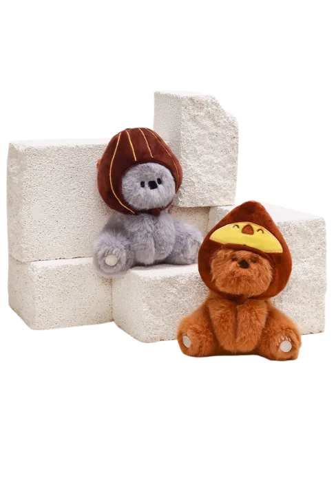 Two plush teddy bear toys with hoods sitting on white textured stone blocks, one gray with chestnut cap, one brown with ye...