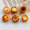 Six miniature resin egg tart charms with cute decorations like cat paw prints and flowers on paper background