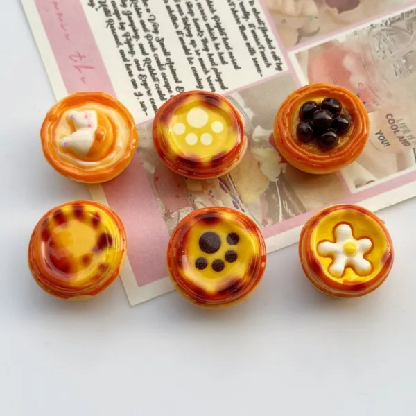 Six miniature resin egg tart charms with cute decorations like cat paw prints and flowers on paper background