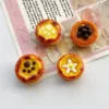 Four miniature egg tart charms with decorative toppings on vintage paper background