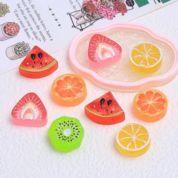 Colorful resin fruit slice charms including watermelon, orange, lemon, kiwi, and strawberry on white surface