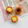 Three miniature egg tart charms with decorative toppings on vintage paper background