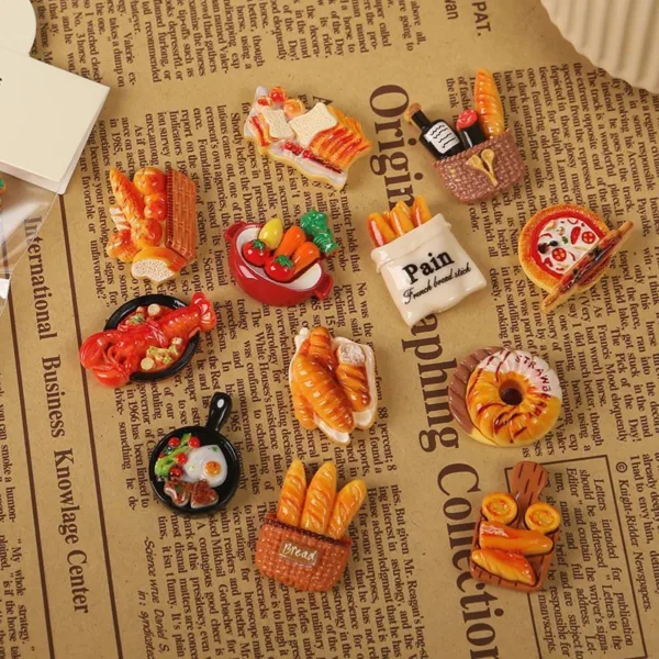 Miniature food magnets featuring bread baskets, pizza, croissants, and cooking pans on newspaper background