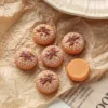 Miniature pineapple bun bread charms on crinkled paper with one showing flat orange back