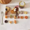 Miniature clay bread and pastry charms arranged on white surface with toast photo and jam jar