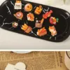 Miniature food charms on black marble tray featuring bread basket, pizza, croissants and Pain sign