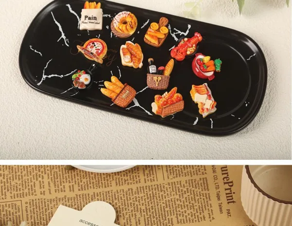 Miniature food charms on black marble tray featuring bread basket, pizza, croissants and Pain sign