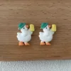 Two cute white duck figurines wearing green hats and holding yellow popsicles on wooden surface