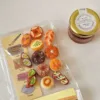 Miniature clay bread and pastry charms on cookbook page next to jar labeled natural