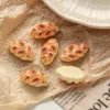Miniature braided bread loaf charms on crinkled parchment paper near white plate