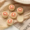 Six Chinese almond cookies with red icing centers on crinkled brown paper and newspaper