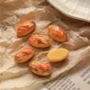 Miniature bread loaf charms with red and yellow toppings on crinkled brown paper