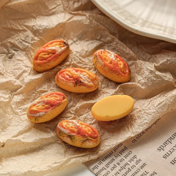 Miniature bread loaf charms with red and yellow toppings on crinkled brown paper